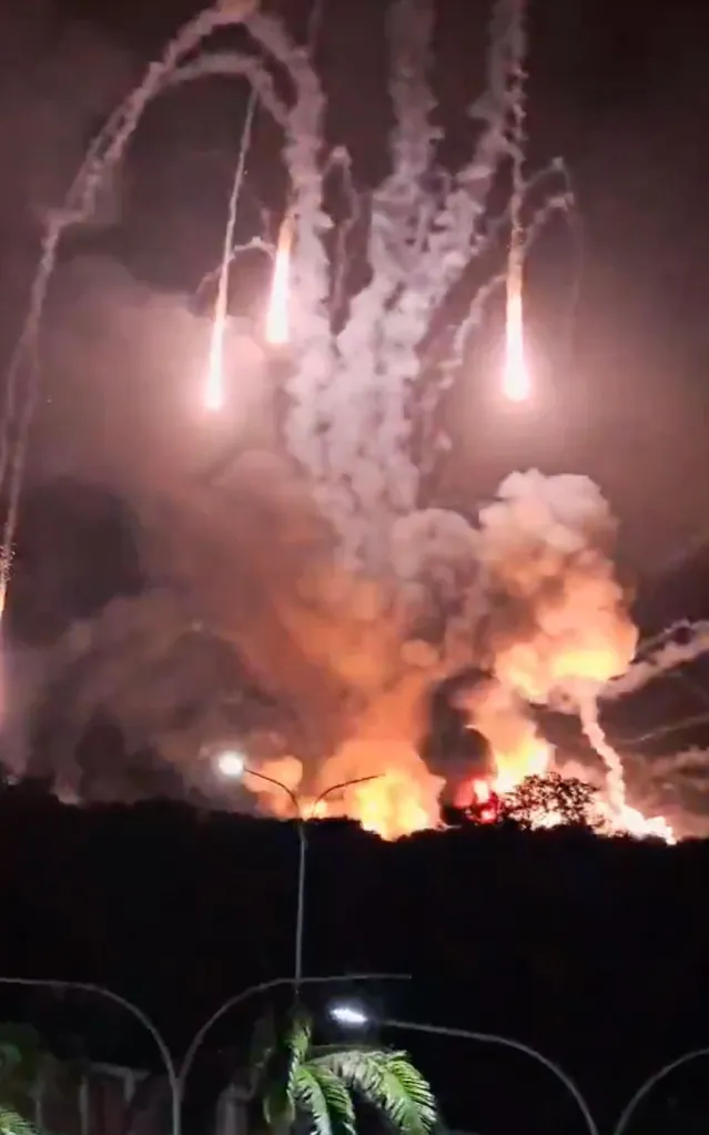 Nighttime image of an airbase being bombed, with explosions and smoke rising into the sky.